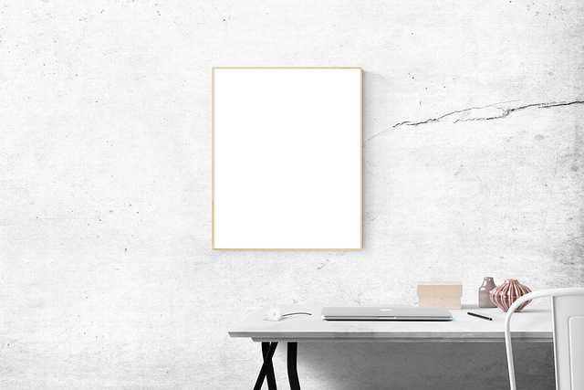 A blank poster frame above a desk with a laptop