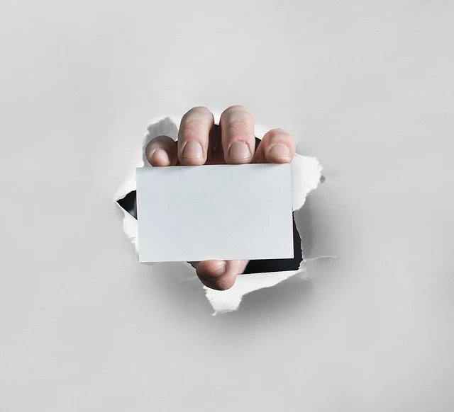 Hand holding a blank card through a torn paper hole