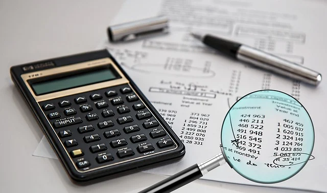 Calculator, pen, and financial documents with numbers under a magnifying glass.