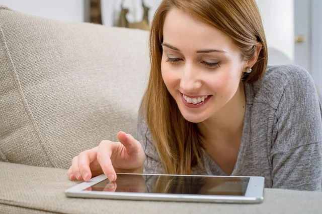 A smiling woman using a tablet, likely browsing or finding information.
