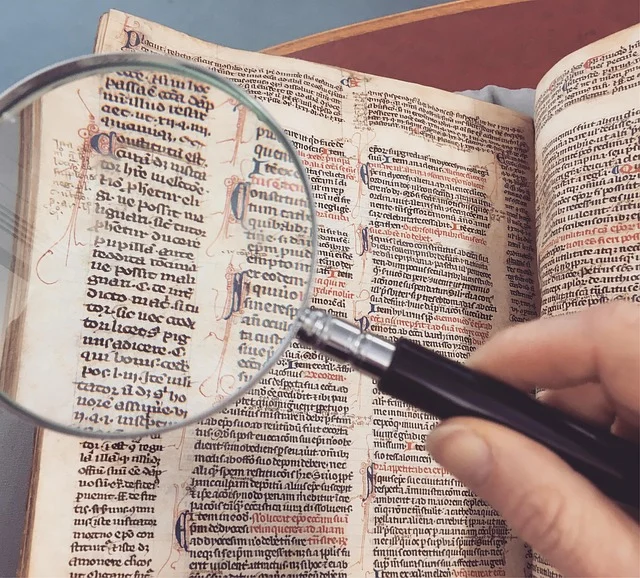 A hand holding a magnifying glass over an old book with text.