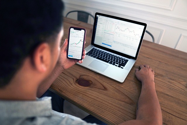 A man looking at stock charts on his smartphone and laptop