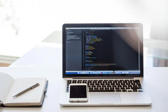 Laptop displaying code, smartphone, and notebook on a desk