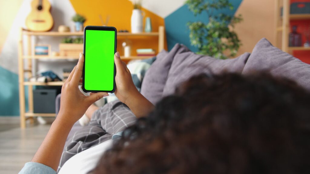 A person holding a smartphone with a green screen on a couch