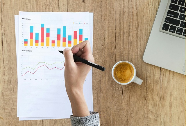 A person reviewing printed financial charts and graphs on a wooden desk