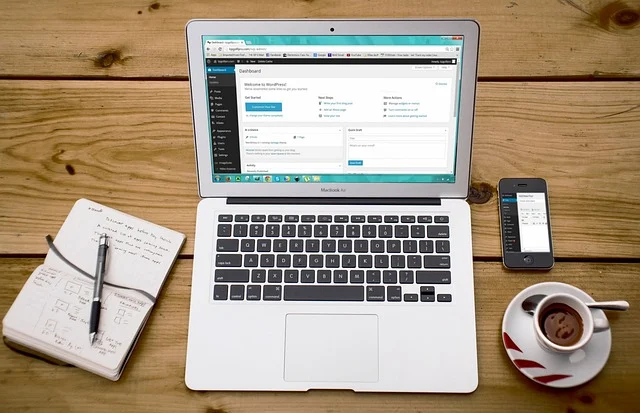 A laptop, smartphone, notebook, and coffee cup on a wooden desk