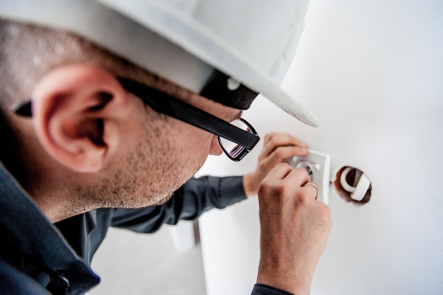 An electrician with a hard hat working on an electrical wall socket