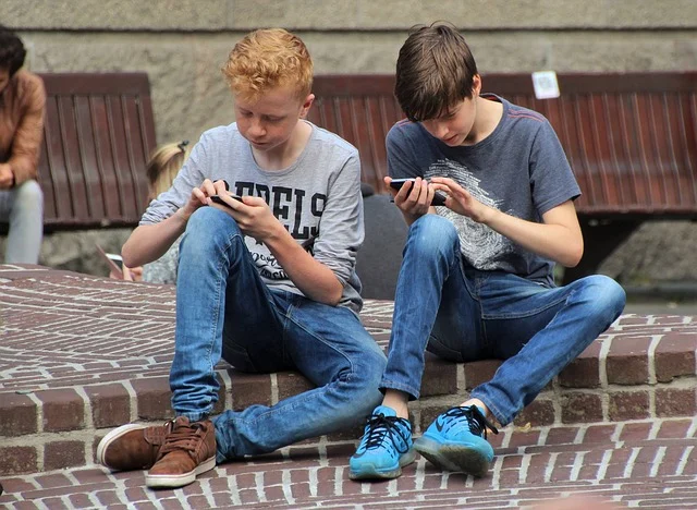 Streaming community: Two boys sitting and looking at their phones, possibly streaming or gaming.