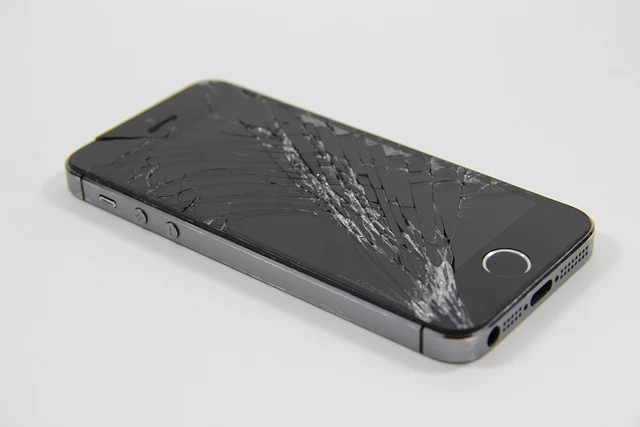 A smartphone with a severely cracked screen, lying on a white surface.